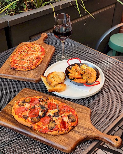Outdoor patio table with red wine and pizza, plus garlic bread and saut&eacute;ed shrimp in a skillet.