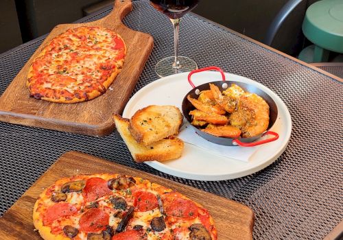 Outdoor patio table with red wine and pizza, plus garlic bread and saut&eacute;ed shrimp in a skillet.