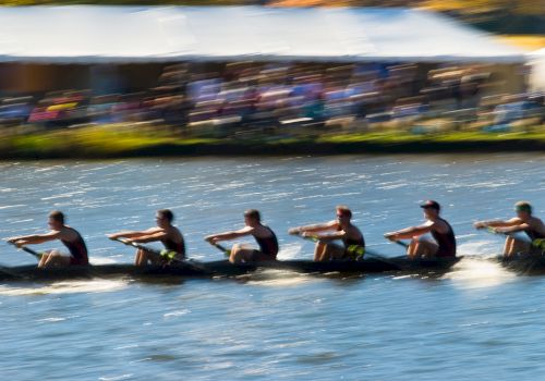 Crew paddling a dragon boat, splashing through the river with sunlight flashing on the water as they race.