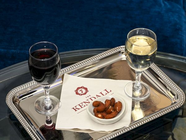 Silver serving tray with two wine glasses and a small bowl of roasted nuts beside a &ldquo;The Kendall&rdquo; napkin, ready for a drink.
