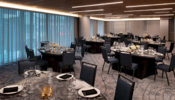 The image shows an elegant banquet hall setup with round tables, chairs, black tablecloths, floral centerpieces, and place settings for a formal event.