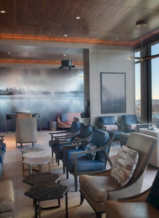 A modern lounge area with comfortable seating, cityscape wall art, floor-to-ceiling windows overlooking a waterfront and a Ferris wheel.