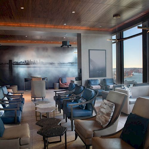 A modern lounge with comfortable seating, large windows offering a scenic view of the sea, and a wall mural in the background.