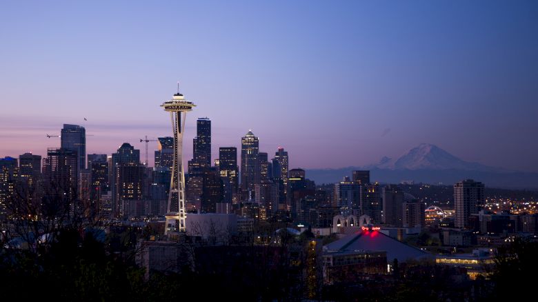 A cityscape at dusk with a prominent tower, numerous high-rise buildings, and a mountain in the background under a clear sky.